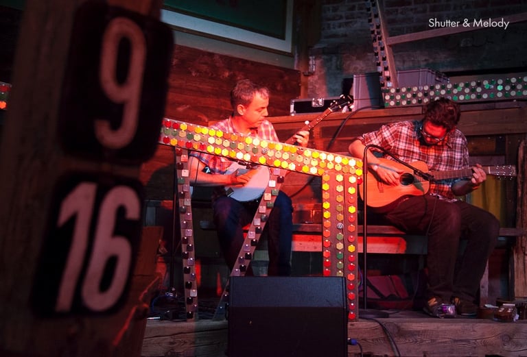 Ein Mann spielt Banjo und ein anderer Gitarre auf der Bühne im Kater.