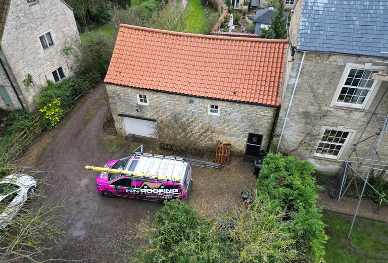 Aerial view of a roofing contractor van parked outside a stone building with a terracotta tile roof.