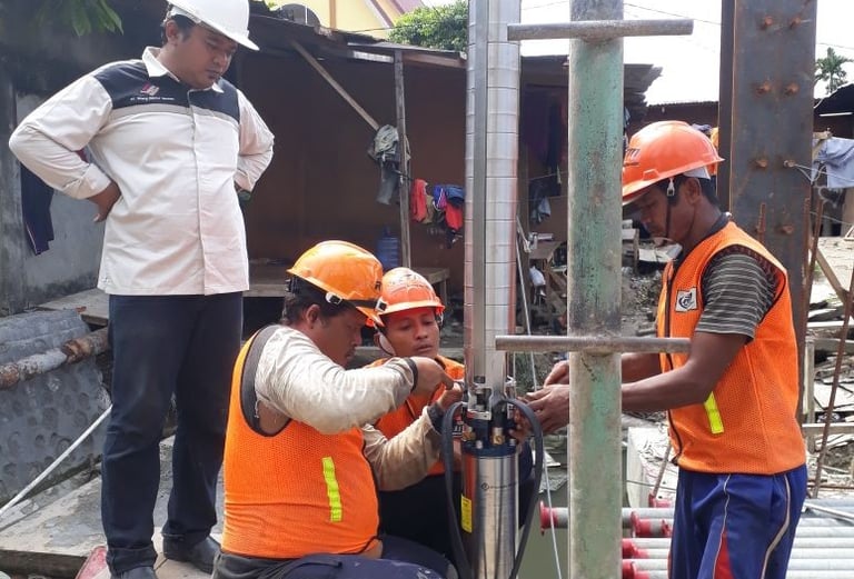 Construction workers in safety gear installing a submersible water pump at an outdoor site.