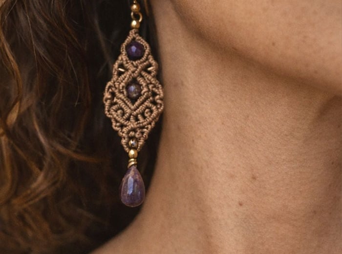 Aretes de macramé marrón con piedras de amatista morada en la oreja de una mujer.