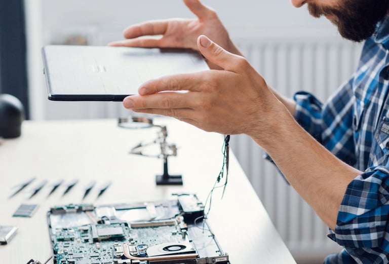 a man holding a tablet computer and pointing at a laptop