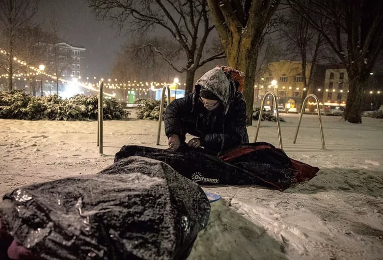 Man sitting in City Hall Park with his belongings in the snow.