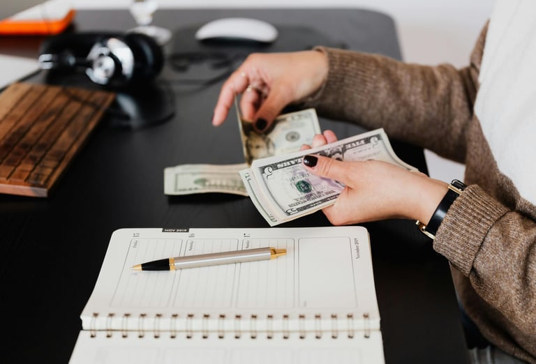 woman holding money in her hand with a pen and paper on desk as she budgets and manages money