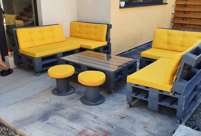 Modern outdoor pallet furniture set with grey wooden frames and bright yellow cushions on a patio.