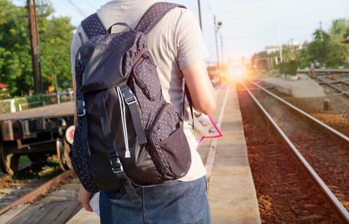 Person with a backpack standing near train tracks, symbolizing a journey, decision, or new direction