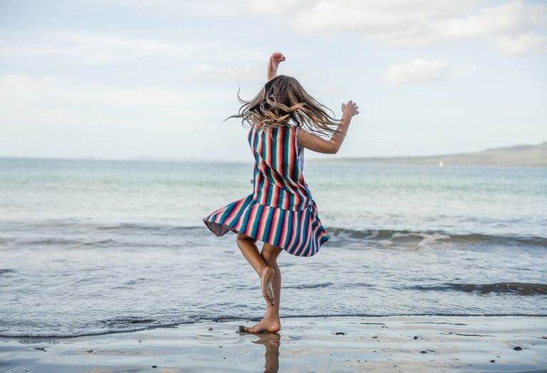 Fashion photography - a girl in a striped dress dancing on the beach