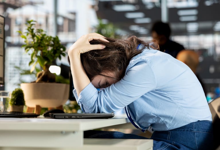 Stressed office worker resting head on desk, illustrating workplace burnout and mental health struggles.