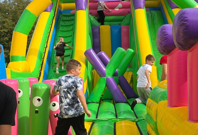 Vaikai aktyviai pramogauja ant didelio, ryškaus pripučiamo kliūčių ruožo, skirto privačioms šventėms