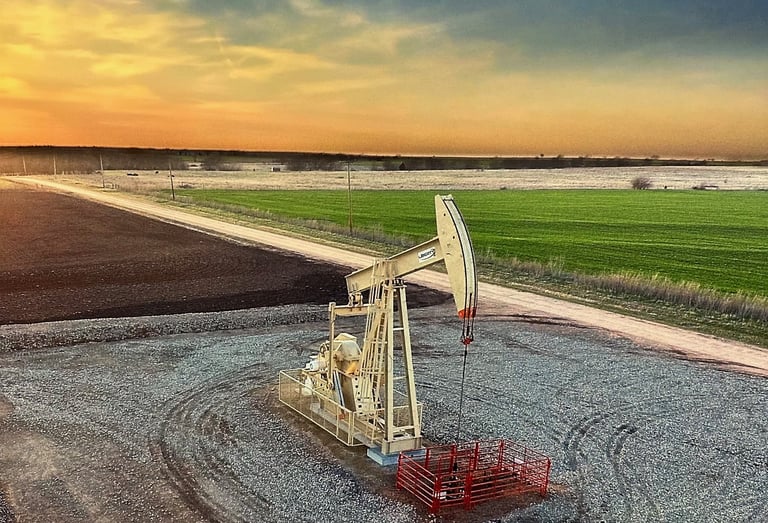 An oil pump jack operates in a rural field during a golden sunset, representing energy production.