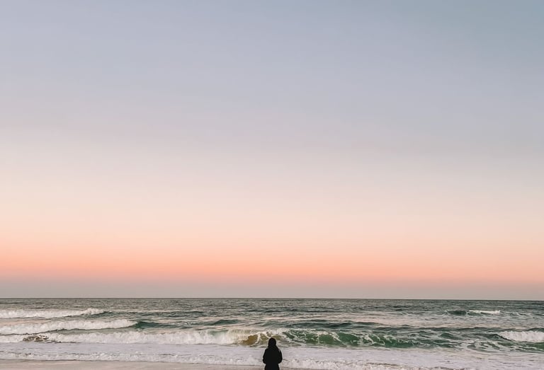 Uma pessoa andando em direção ao mar, de costas, ao por do sol.