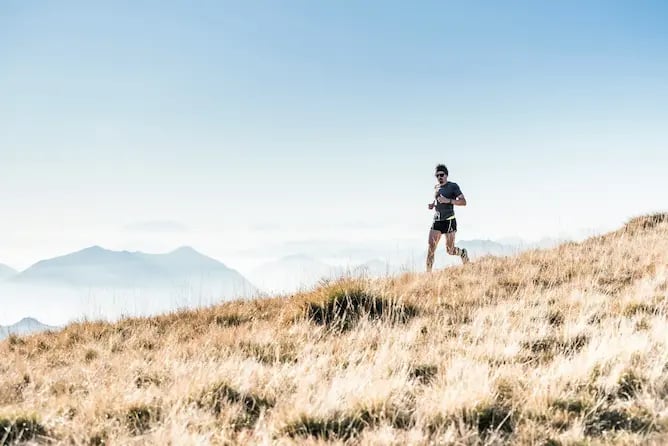 Coach de trail en montagne courant sur un sentier, illustrant le coaching course et trail en ligne