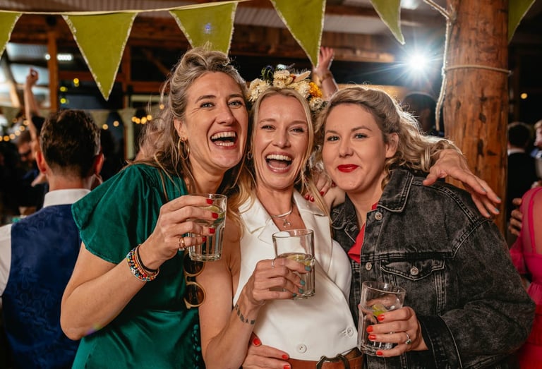 Bride and friends laughing with drinks during South Wales wedding reception, captured in candid style by photographer Owen Ma