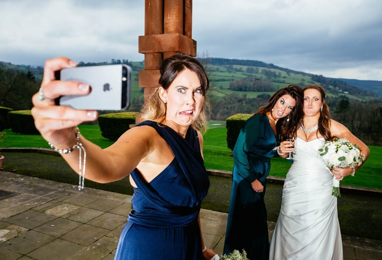 Bridesmaid taking funny selfie with bride and guest at South Wales wedding, captured candidly by photographer Owen Mathias