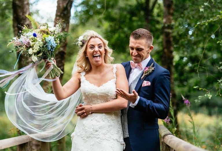 Bride and groom laughing on wooden bridge at Llanerch Vineyard wedding in South Wales, captured candidly by Owen Mathias