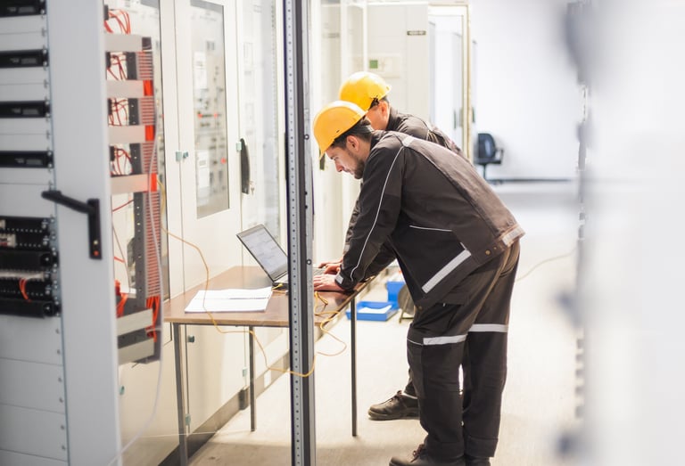 Technicians in hard hats using a laptop for electrical maintenance.