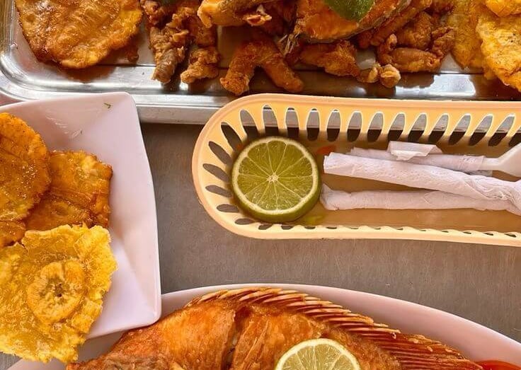 Crispy fried whole tilapia served with golden tostones, rice, and fresh salad garnish.