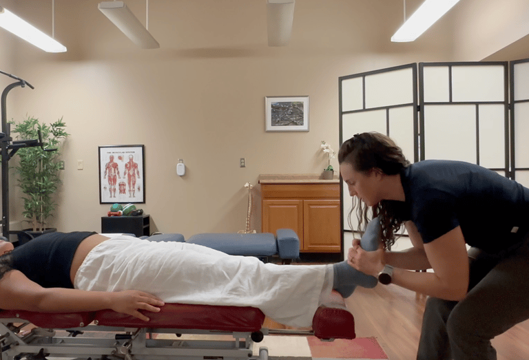 Chiropractor adjusting patient's foot while patient lays on back on chiropractic table. 