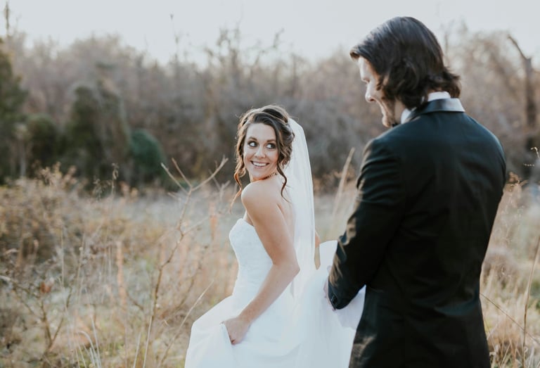 Besišypsanti nuotaka su nėrinių suknele ir nuometu eina lauku su jaunikiu.