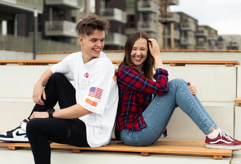 Lachendes Paar sitzt Rücken an Rücken auf einer Bank. Urbanes Paarfoto von Just Perspectives.