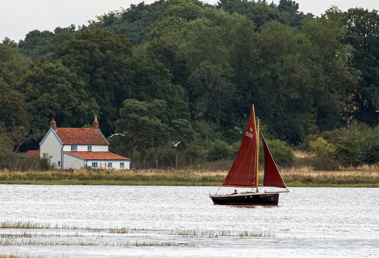 a sailboat in the water with a house in the background taken by Pixel Perfect Photography