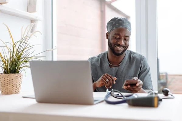 a pharmacy man sitting at a desk with a laptop and a cell phone