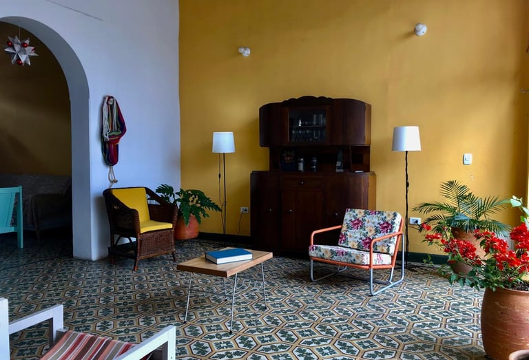 Eclectic living room with vintage furniture, yellow accent wall, and patterned tile flooring.