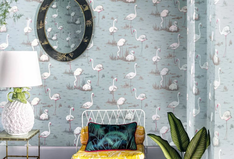Chic interior featuring pink flamingo wallpaper, a vintage oval mirror, and a tropical lounge chair.