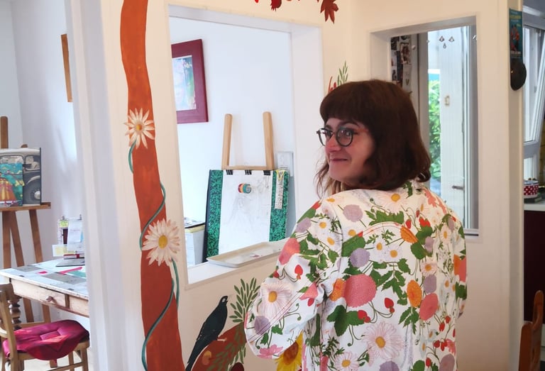 Photo de l'artiste-peintre Marie Hardy devant une fresque d'arbre réalisée dans le salon d'un particulier en Normandie