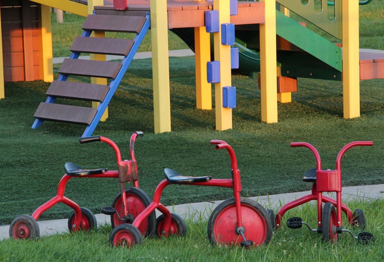 Colorful pieces of a playground for kids with 3 little red tricycle bikes parked in the foreground.
