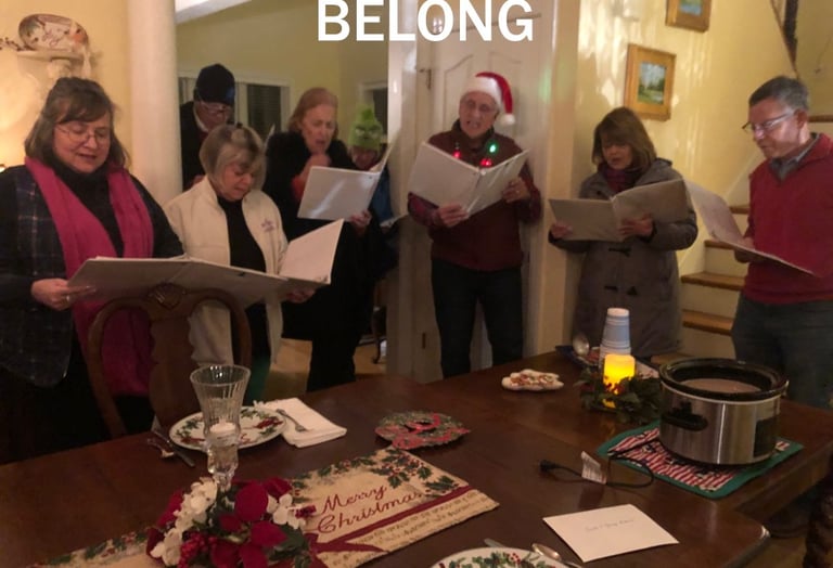 Group of seven adults singing Christmas carols around a table.
