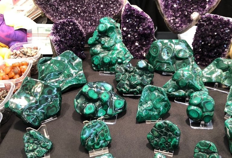 Polished green malachite stones and amethyst specimens displayed at a gem and mineral show.