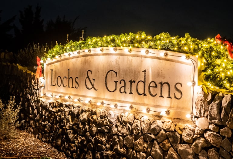 A stone sign with illuminated by warm white string lights at night, highlighting the entrance to a festive