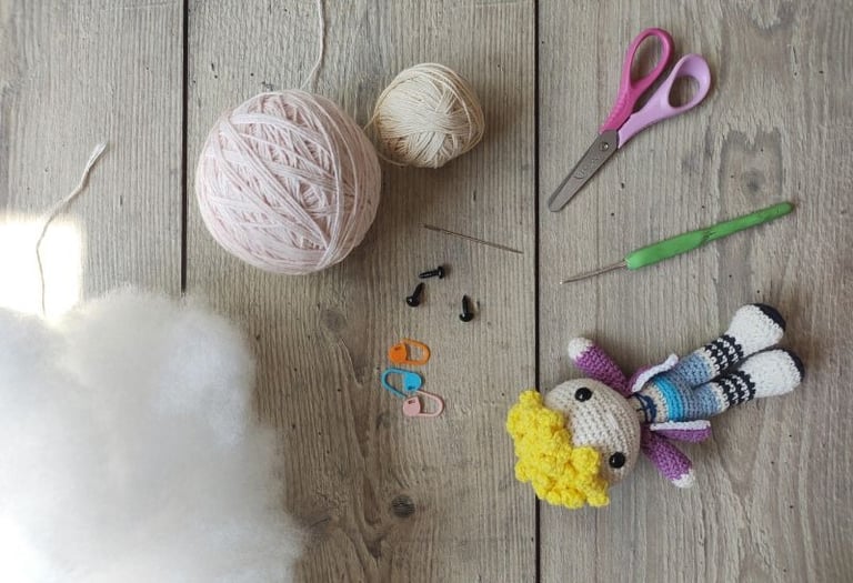 Crochet amigurumi kit with yarn, stuffing, hook, and a handmade doll on a wooden surface.