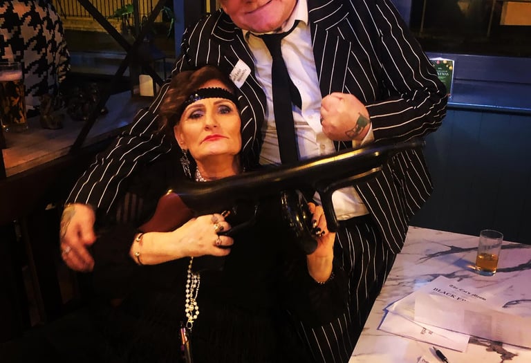 older man and woman at a murder mystery. the woman is holding a gun.