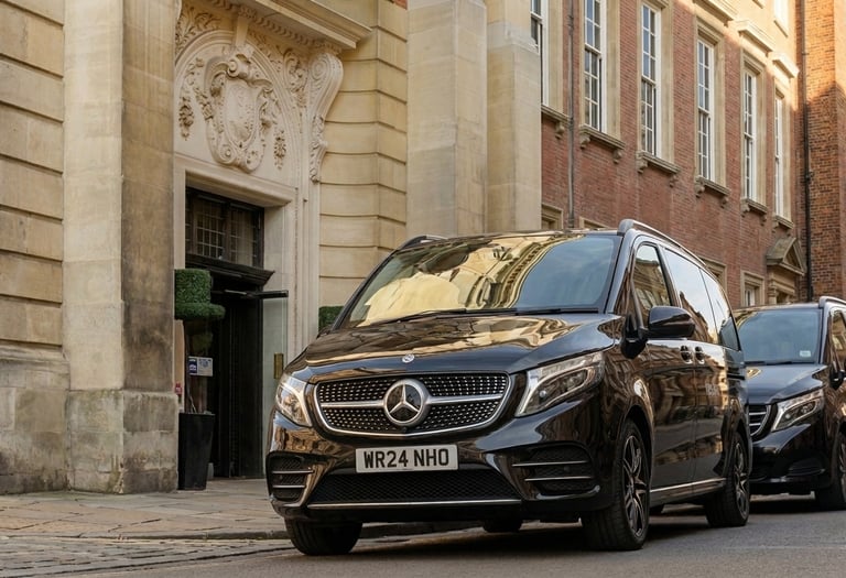 Black Mercedes-Benz V-Class chauffeur cars parked outside a historic stone building in York.