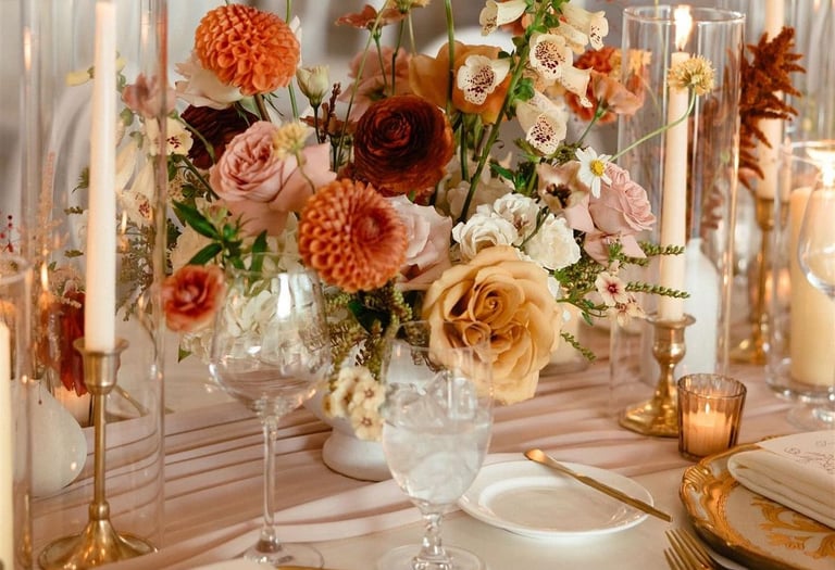 Mesa elegante con vajilla dorada, velas altas y arreglo floral sofisticado.