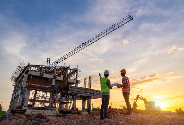 Civil engineers wearing safety helmets inspecting a building construction site at sunset with a crane.
