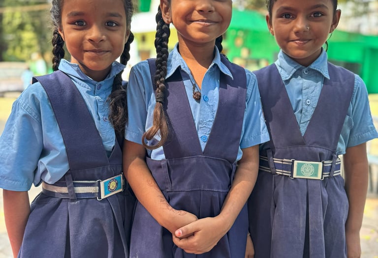 Three young schoolgirls in blue uniforms standing together smiling outdoors
