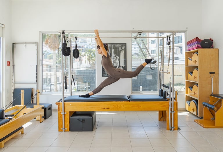 Woman doing a split stretch on a Pilates Cadillac apparatus in a bright studio in Cabo San Lucas.