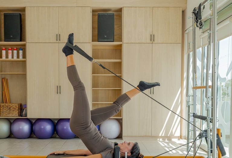 Woman lying on a Pilates Reformer doing a leg exercise using the foot straps in the Cabo San Lucas studio.
