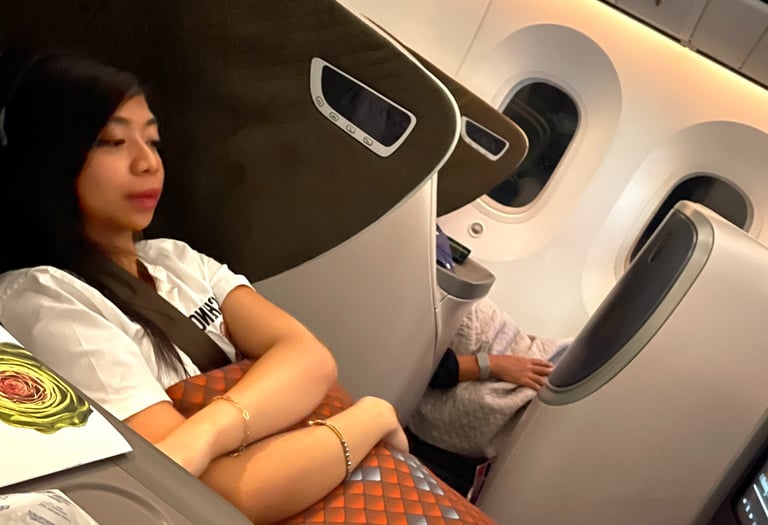 a woman laying down on a lie-flat business class seat in a plane while watching a movie