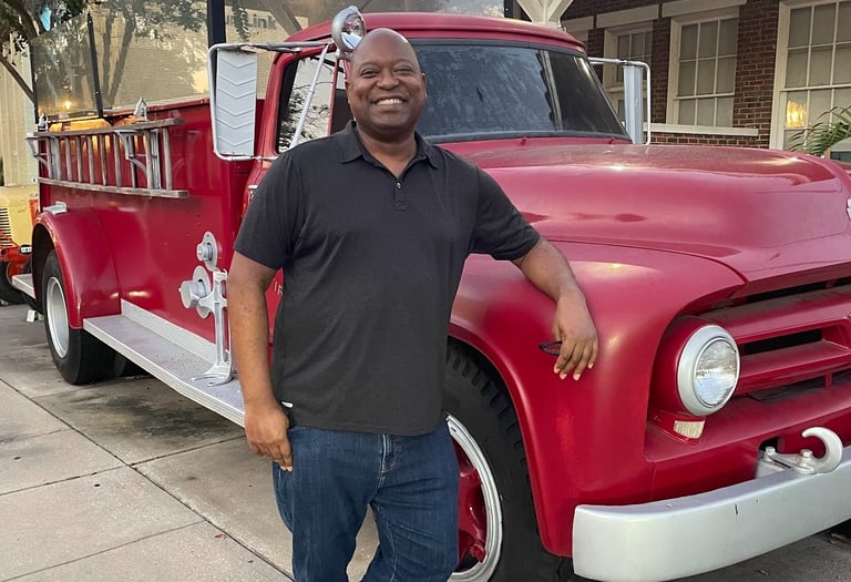 Photo of attractive dark skinned male leaning against a vintage red fire truck