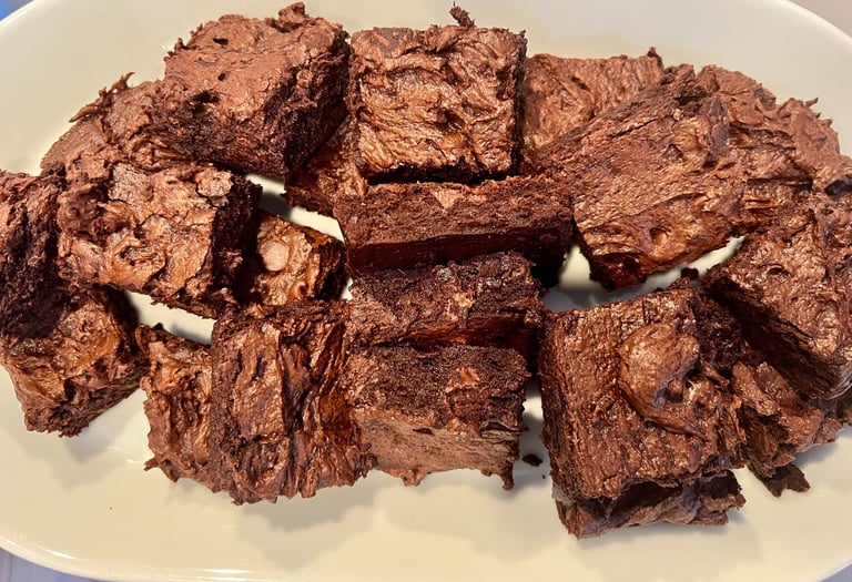 A white plate filled with squares of rich, fudgy chocolate brownies featuring a crinkle top.