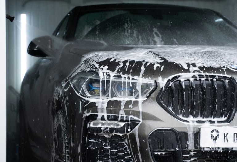 soapy front grill, lights and bumper of a grey bmw that is dripping wet with soap running down.