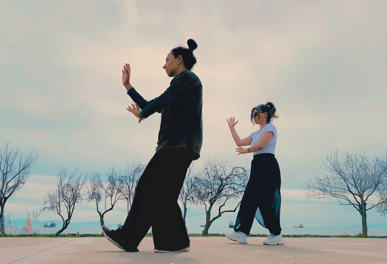 Ebru Tütek and student practicing Bagua walking by the sea, with bare trees and ships in the distance.
