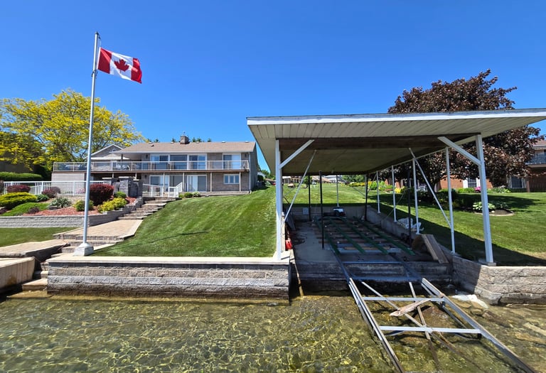 Waterfront cottage in Canada with a boat lift, private dock, and Canadian flag under a clear blue sky.