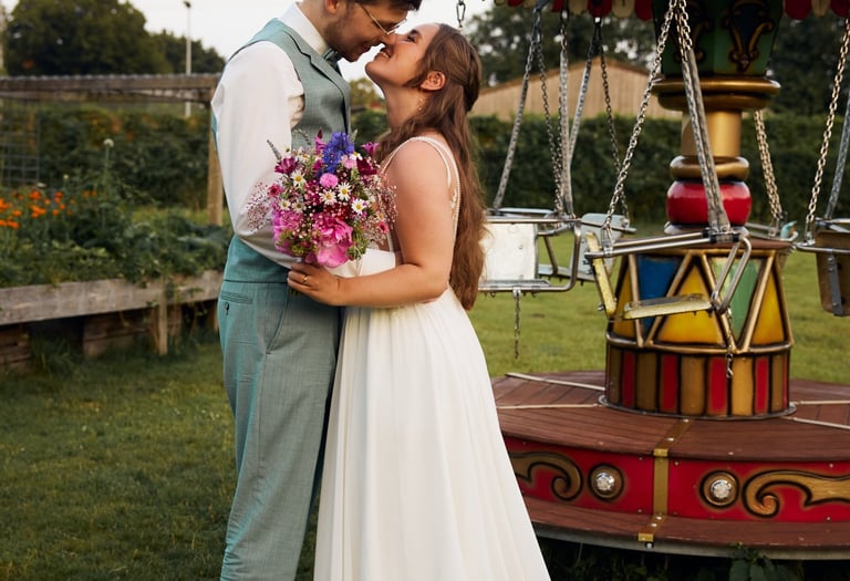 A bride and groom sharing a romantic moment by a vintage carnival carousel at their outdoor wedding.