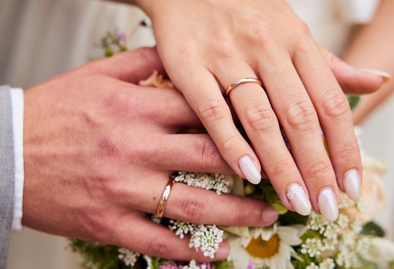 Close-up of a bride and groom's hands with gold wedding rings resting on a floral bridal bouquet.