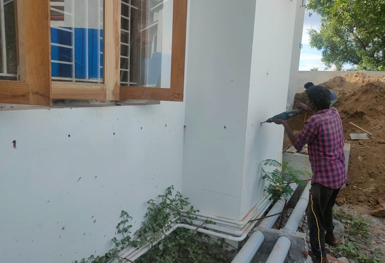 Professional pest control technician drilling exterior walls for termite treatment near a house window.