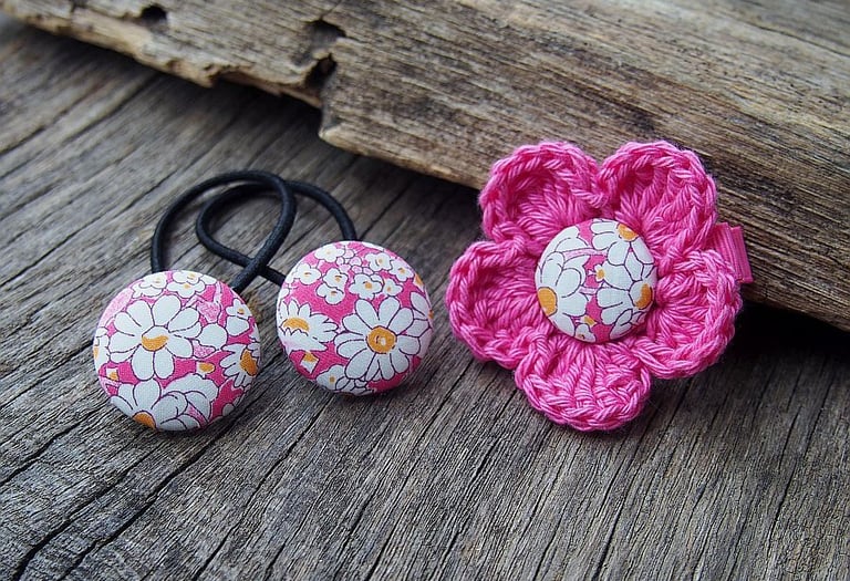 różowy zestaw gumek do włosów i spinki z kwiatkiem na tle drewnianej deski